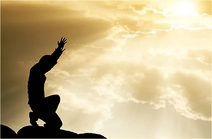 Silhouette of a person kneeling with arms raised against a bright, cloudy sky.