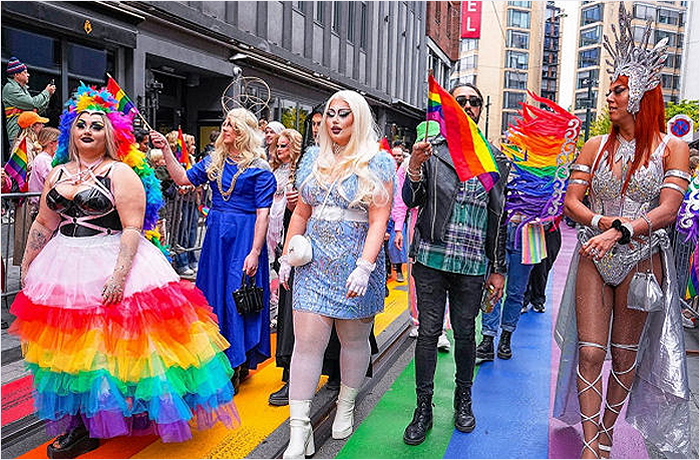 A vibrant LGBTQ+ pride parade featuring a diverse group of participants dressed in colorful outfits, celebrating with rainbow flags and accessories on a rainbow-colored street.